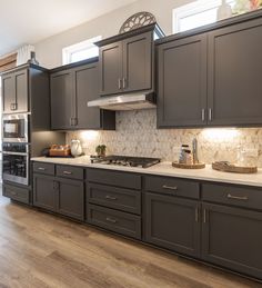 a kitchen with dark gray cabinets and white counter tops, wood flooring and stainless steel appliances