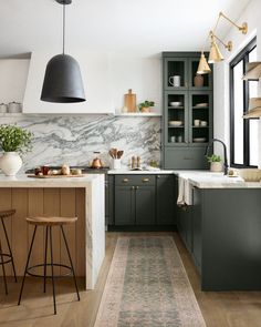 a kitchen with gray cabinets and marble counter tops, an area rug on the floor