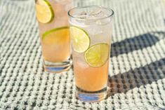 two glasses filled with lemonade and limes on top of a tableclothed cloth