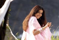 a woman in a pink sari pointing at something with her right hand and smiling