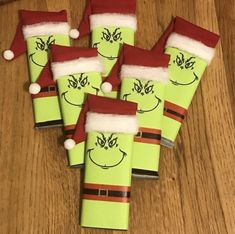 six green wrapped presents with santa hats and grin face drawn on them sitting on a wooden table