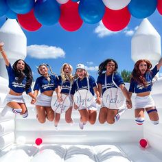 a group of women in cheerleader outfits jumping into the air with red, white and blue balloons