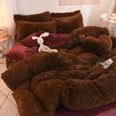 a bed covered in brown fur with a stuffed animal on it's back and pillows