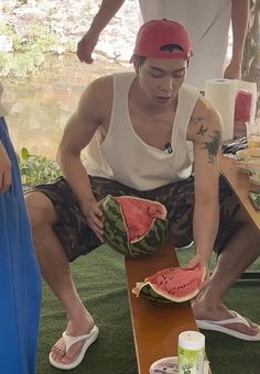 a man sitting on top of a wooden table next to a watermelon