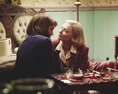 two women sitting at a table talking to each other in a room with green walls