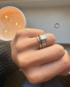 a person's hand with a ring on it next to a cup and candle