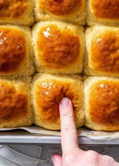 a hand pointing at some bread rolls in a pan