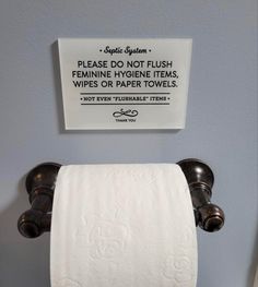 a sign on the wall above two rolls of toilet paper that are not in use