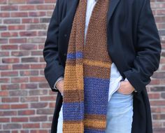 a man standing in front of a brick wall wearing a brown and blue striped scarf