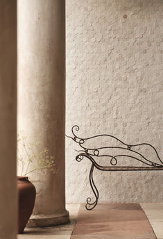 a wrought iron bench sits in front of an old pillar and planter on the floor