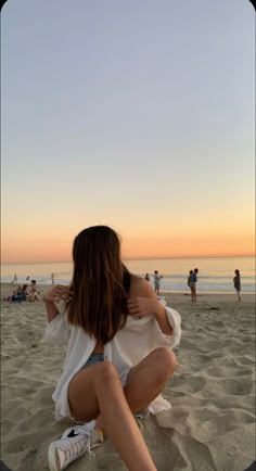 a woman sitting on top of a sandy beach next to the ocean with people in the background