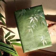 a hand holding a green notebook with bamboo leaves on it