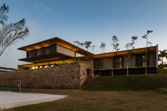 a modern house with stone walls and palm trees in the background at dusk, lit up by lights