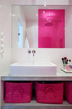 a bathroom sink with two pink baskets underneath it