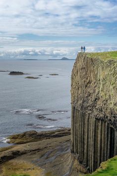 two people are standing on the edge of a cliff overlooking the ocean and cliffs below