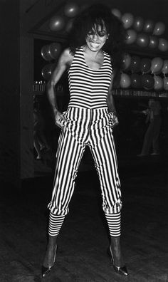 a black and white photo of a woman in striped pants with her hands on her hips