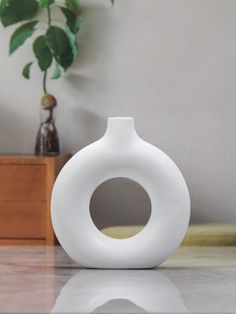 a white vase sitting on top of a wooden table next to a potted plant