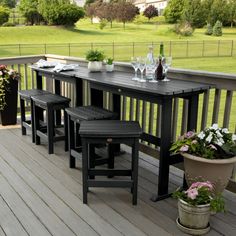 an outdoor table with four stools on a deck next to potted plants and wine bottles