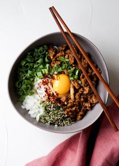 a bowl filled with rice, meat and veggies next to chopsticks