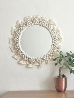 a round mirror hanging on the wall next to a potted plant in a vase