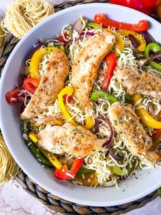 a white bowl filled with chicken, peppers and noodles next to some sliced oranges