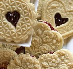 heart shaped cookies with jam in the middle on a white plate next to another cookie