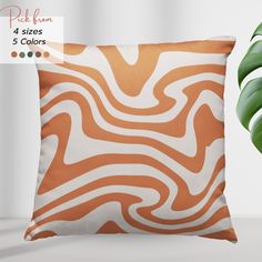 an orange and white pillow sitting next to a green plant