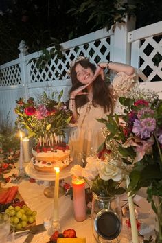 a woman standing in front of a table filled with food and flowers next to candles