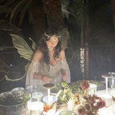 a woman dressed as a fairy preparing food at a table with candles and flowers on it