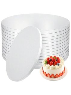 a white cake with fruit on top next to stacks of plates