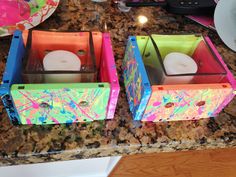 two colorful boxes sitting on top of a counter next to a plate with a candle in it