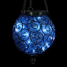 a blue glass ball hanging from chains on a black background with the light reflecting off it's side