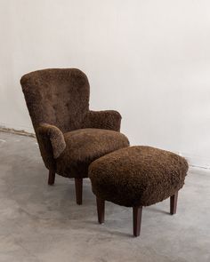 a brown chair and ottoman sitting on top of a cement floor next to a white wall