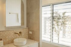 a white sink sitting under a bathroom mirror next to a window with shutters on it