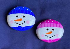 two painted rocks with snowmen on them sitting next to each other in front of a blue background