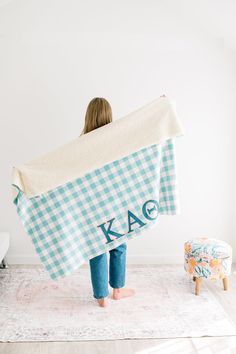 a woman is holding up a blanket with the letters kae on it in front of her