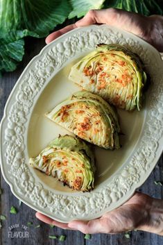 three pieces of artichoke on a white plate with hands holding one piece and the other half