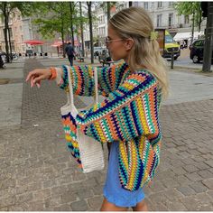 a woman is walking down the street carrying a crocheted purse