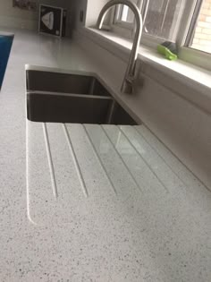 a kitchen sink sitting under a window next to a blue counter top in front of a window