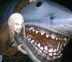 a man is posing next to a fake shark with his mouth open and teeth out