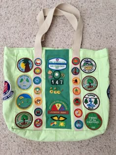 a green tote bag with many different badges on the front and side, sitting on a carpeted floor