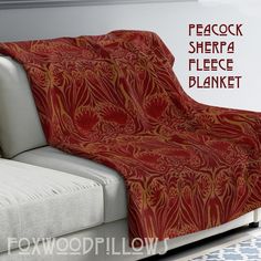 a couch covered in a red and gold blanket next to a wall with the words peacock sherpa fleece blanket on it