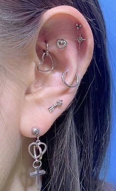 a close up of a person wearing ear piercings with an anchor, cross and heart