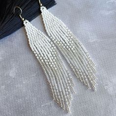 the white beaded fringe earrings are hanging off of a piece of black fabric on top of