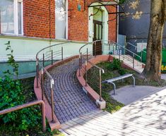 a brick building with stairs leading up to the front door and an empty bench next to it