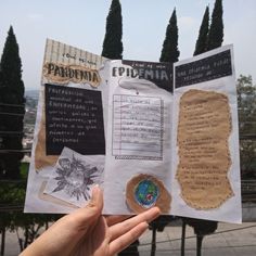 a person holding up a book with pictures and words on it in front of some trees