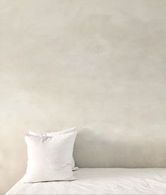 a bed with white sheets and pillows against a wall