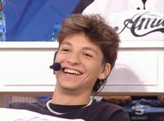 a young man wearing a headset smiles at the camera while sitting in front of an audience