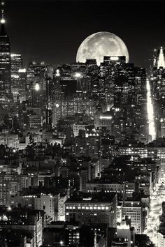 black and white photograph of city skyline at night with full moon in the sky above