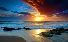 the sun is setting over the ocean with waves coming in to shore and rocks on the beach